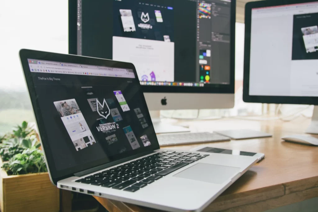 Cara membuat website company profile untuk perusahaan: meja kerja dengan laptop dan monitor menampilkan desain website bisnis