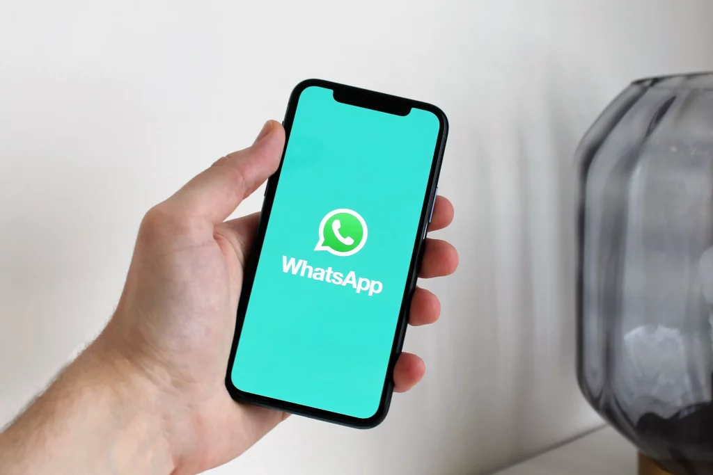 Chatbot WhatsApp untuk customer service: tangan memegang smartphone dengan layar aplikasi WhatsApp sebagai ilustrasi layanan pelanggan otomatis
