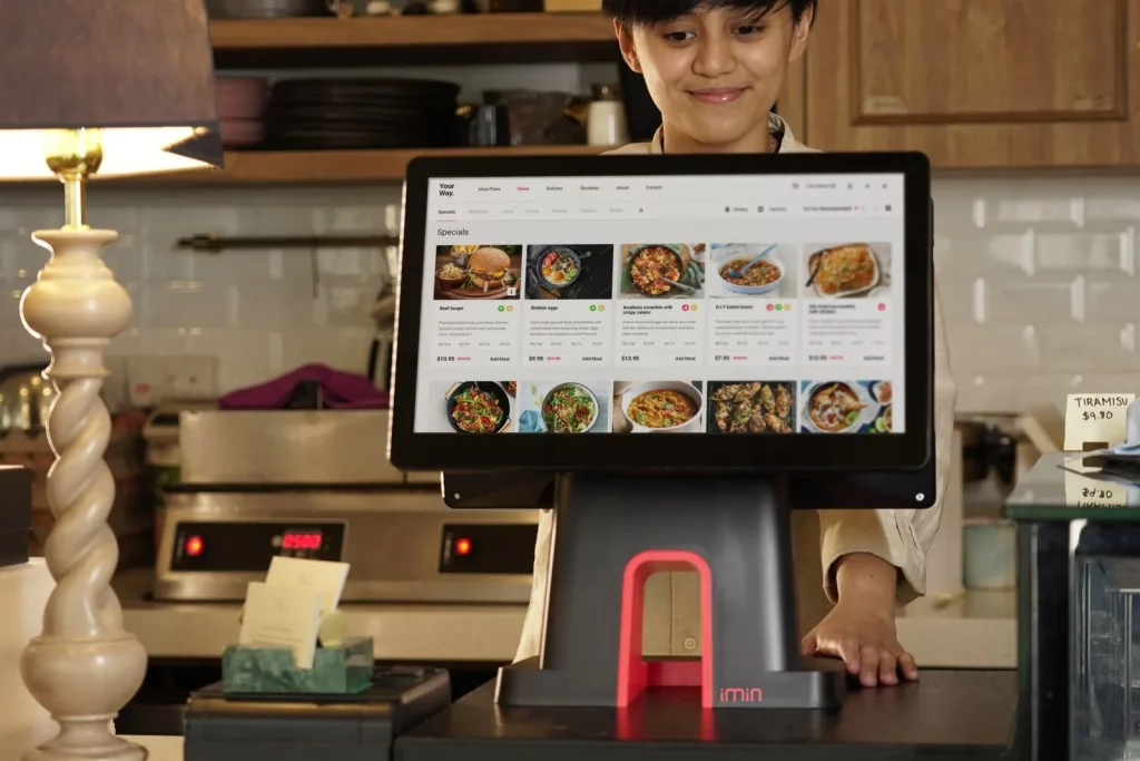 Kasir restoran mencatat pesanan pelanggan memakai aplikasi kasir digital di layar sentuh