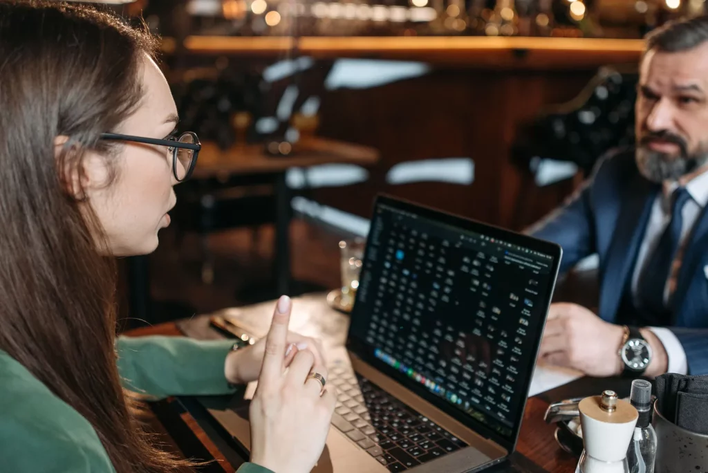 Ilustrasi aplikasi restoran multi cabang: diskusi manajemen dengan laptop di restoran untuk memantau stok dan laporan beberapa outlet