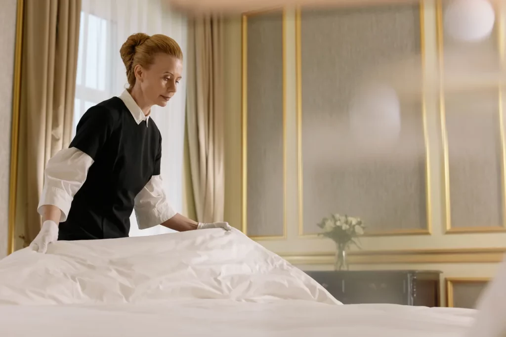 Petugas housekeeping hotel merapikan tempat tidur di kamar, ilustrasi aplikasi inspeksi hotel dan housekeeping untuk menjaga standar kebersihan kamar