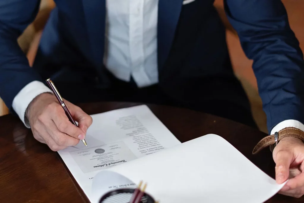 Dua orang menandatangani dokumen perjanjian di meja kerja, ilustrasi pemakaian e-Meterai untuk dokumen perusahaan secara digital